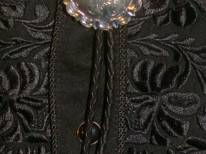 A close up of a black jacket with a "Rex" Large Silver western bolo tie.