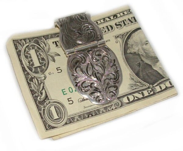 A Silver Engraved Fold Over Western Money Clip is sitting on top of a dollar bill.