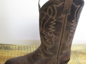A "Denver" Mens 10.5 WIDE brown leather cowboy boot on a wooden table.