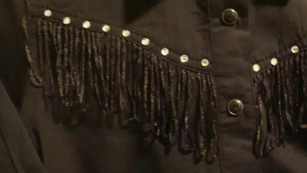 A black shirt with fringes hanging on a hanger.