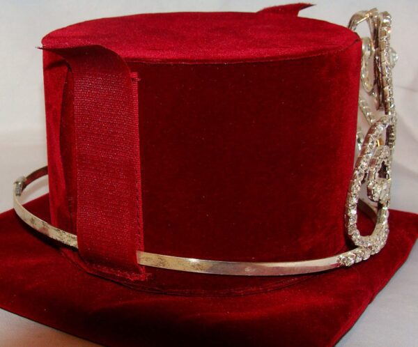 A Cowboy Hat Tiara Crown Carrying Case with Shoulder Strap is sitting on top of a red velvet.
