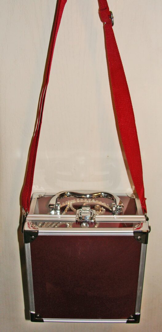 A Cowboy Hat Tiara Crown Carrying Case with Shoulder Strap in burgundy with a red strap hanging on a wall.