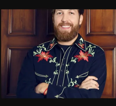 A bearded man in a floral shirt is posing for a photo wearing the "Christmas Poinsettia" Mens Scully Black Western Shirt.