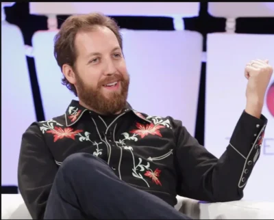 A man in a "Christmas Poinsettia" Mens Scully Black Western Shirt is sitting on a chair and raising his fist.