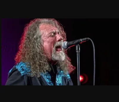 A man with long hair wearing a "Turquoise Gunfighter" Mens Turquoise Embroidered Western shirt singing into a microphone.