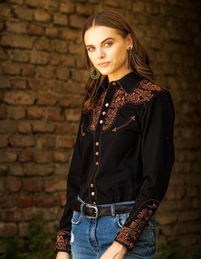 A woman wearing a Big Iron Scully Womens Black Embroidered Western Shirt with snaps and jeans.