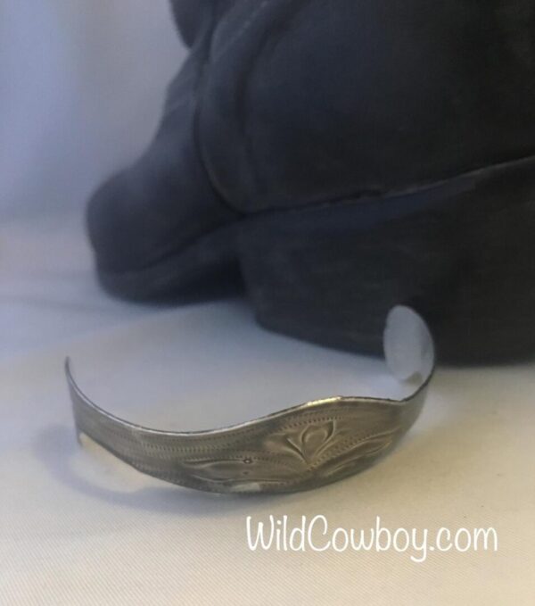 A silver cuff bracelet beside a pair of Laser Etched Antique Silver Cowboy Boot Heel Guards.