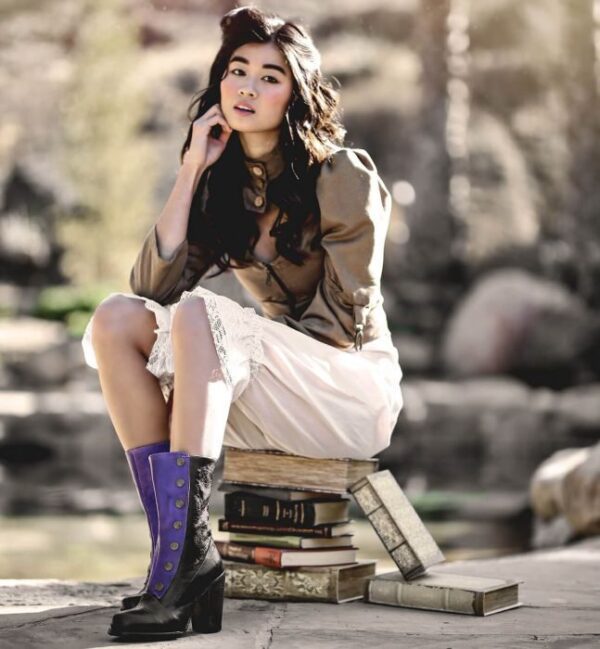 A woman sitting on a pile of books with Amelia Poison Leather Button Snap Womens Purple Zip Granny Boots.