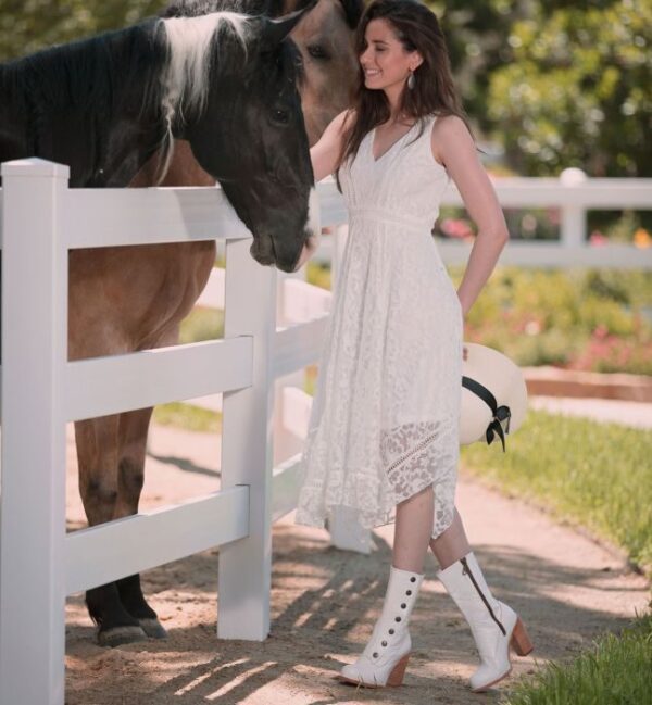 A woman in Amelia Off White Leather Button Snap Womens Zip Granny Boots standing next to a horse.