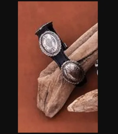A pair of Silver Concho Leather Western Bracelets on a piece of wood in a western style.
