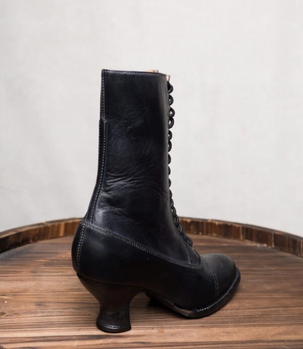 A pair of Mirabelle Black Leather Womens Granny Boots on top of a wooden barrel.
