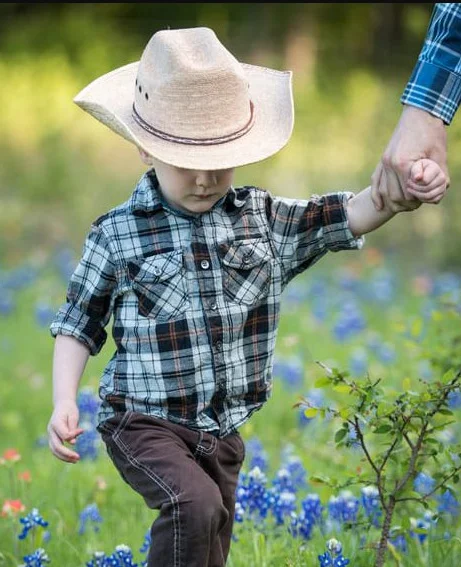 A young boy wearing a cowboy hat walks through a field of bluebonnets.