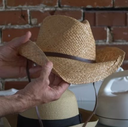 A man is putting on a straw cowboy hat.