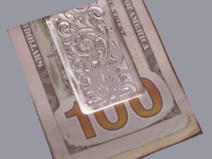The Silver Scroll Wide Engraved Western Money Clip elegantly rests on top of a 100 dollar bill.